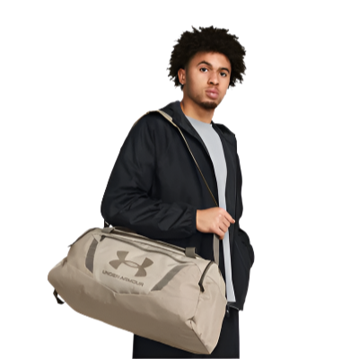 Man holding Under Armour UA Undeniable 5.0 Small Duffle Bag in beige, showcasing its lightweight and durable design.